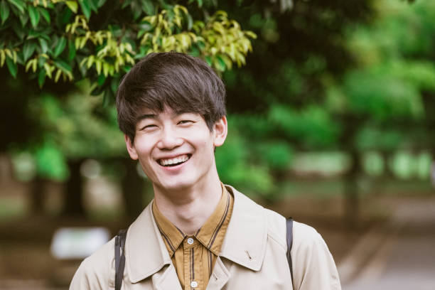 Portrait of cheerful Japanese young man smiling Handsome Asian man with brown hair in his 20s looking at camera raincoat photos stock pictures, royalty-free photos & images