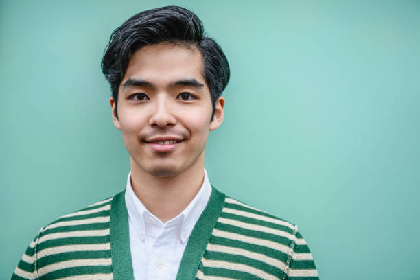 Portrait of attractive young Japanese man in green and white striped cardigan Young Asian man with quiff hair in his 20s smiling towards the camera against a mint green plain background rockabilly hair men stock pictures, royalty-free photos & images