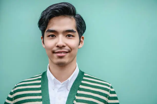 Young Asian man with quiff hair in his 20s smiling towards the camera against a mint green plain background