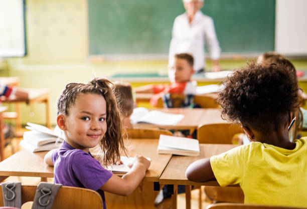 istock Smiling school girl having a class with her friends in the classroom. 1150475721