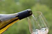 White wine pouring from a bottle into the glass on green nature blurred background