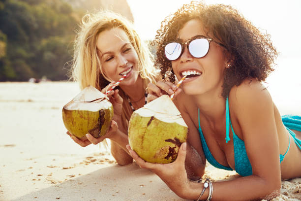 istock Smiling women suntanning on a beach and drinking from coconuts 1150483642