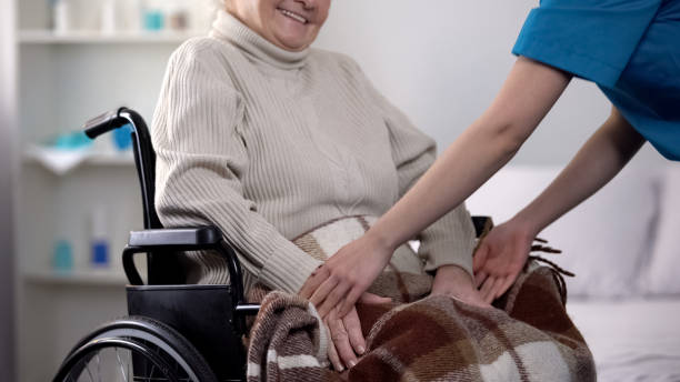 enfermera cubriendo suavemente con la mujer manta en silla de ruedas, se preocupan por los ancianos - women middle aging process covering fotografías e imágenes de stock