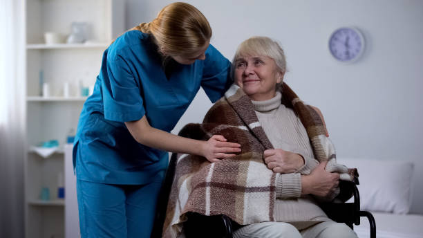 enfermera amable cubriendo con una manta discapacitada, atención hospitalaria, servicio - women middle aging process covering fotografías e imágenes de stock