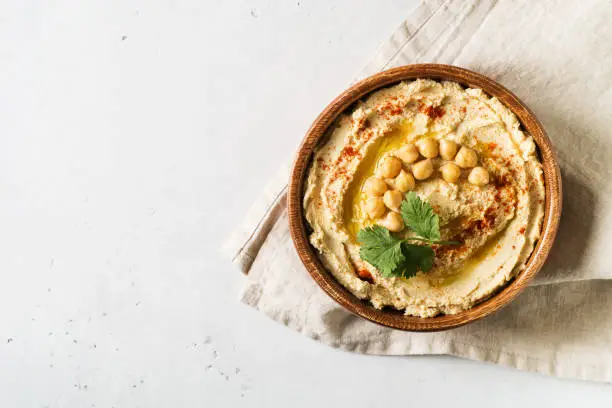 Hummus dip with chickpea, and parsley in wooden plate on white background . Top view, copy space