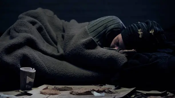 Photo of Homeless person covered by blanket sleeping on city street, poverty concept