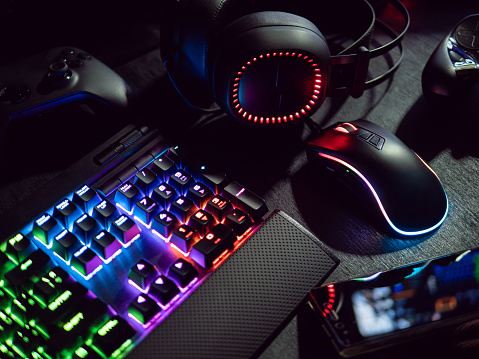 gamer workspace concept, top view a gaming gear, mouse, keyboard with RGB Color, joystick, headset, webcam, VR Headset on black table background.