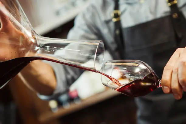 Sommelier pouring wine into glass from decanter. Male waiter pour out alcohol beverage into wineglass at bar counter. Bartender at work