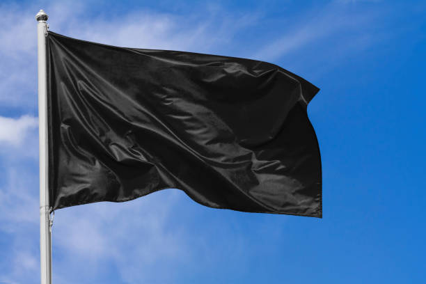 istock Black flag waving in the wind on flagpole against the sky 1150498296