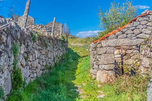 View of pedestrian path up through agricultural fields, with buildings and walls in granitic stone, built in a traditional way, in the Caramulo mountains, Portugal
