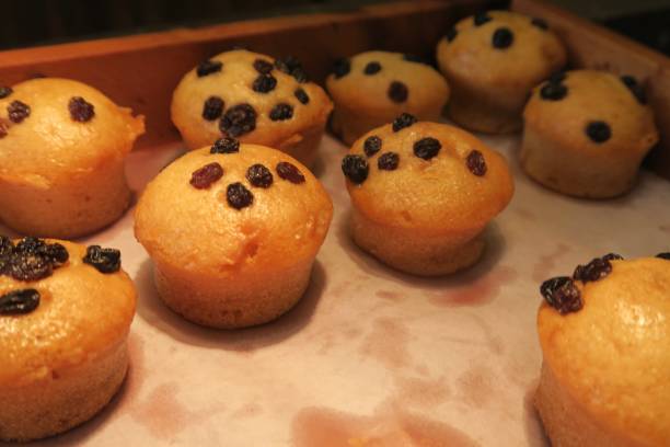 Stock photo showing homemade chocolate chip eggless breakfast mini muffins cakes, The muffins are topped with tutti frutti and bakery cupcakes on greaseproof paper in wooden tray, baked muffins on baking tray served as part of restaurant breakfast buffet at hotel in Delhi, India imagen de chocolate casero sin eggless desayuno mini magdalenas tortas cubiertas con tutti frutti, magdalenas de panadería en papel a prueba de grasa en bandeja de madera, muffins horneados en bandeja de hornear, restaurante desayuno en el hotel, delhi, i