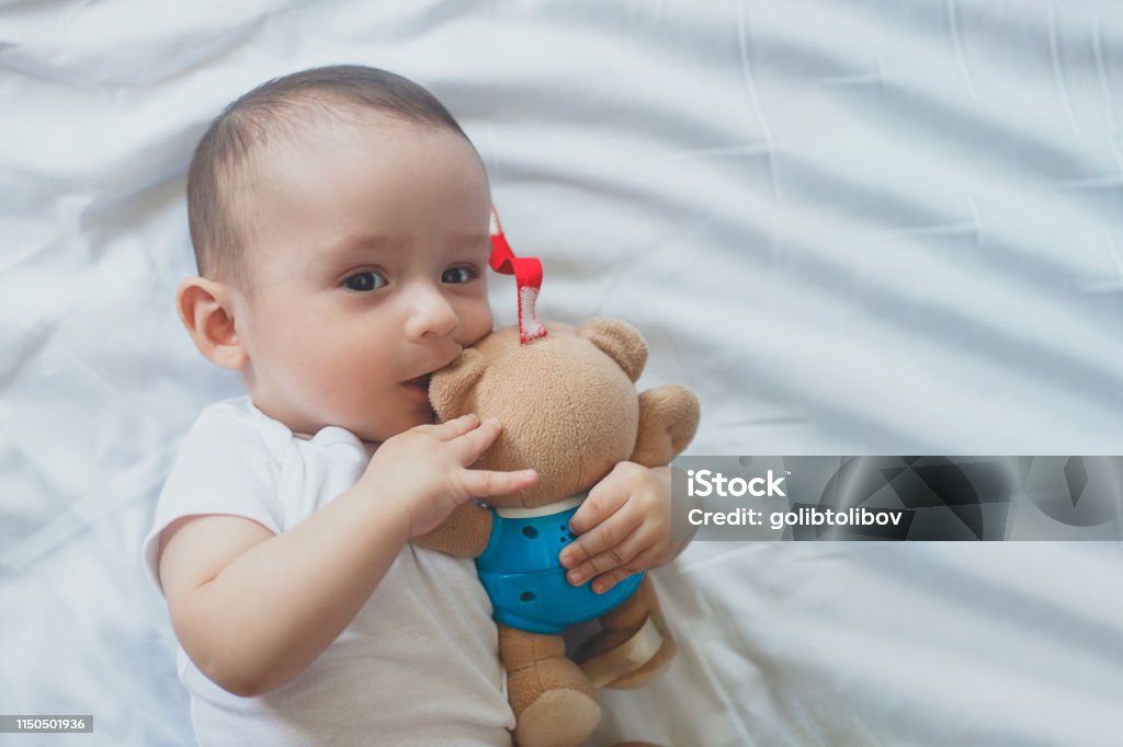 6-8 month old baby boy lying playfully in bed 6-8-month-old baby boy lying playfully in bed. Charming 6-7 month little baby in white bodysuit. Baby boy in white bedding. Free space 0-11 Months Stock Photo