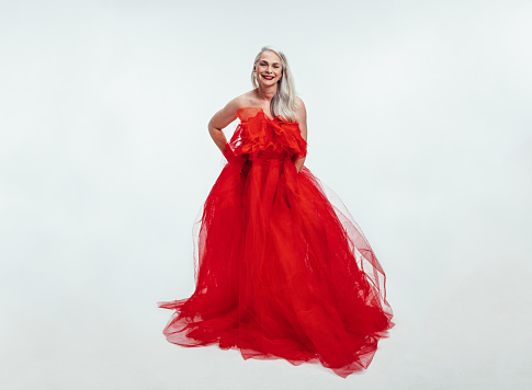 Full length of beautiful senior woman in a red evening gown over white background. Senior woman posing in a gorgeous gown.