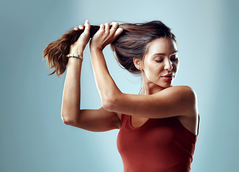 Studio shot of an attractive young woman pulling her hair against a blue background