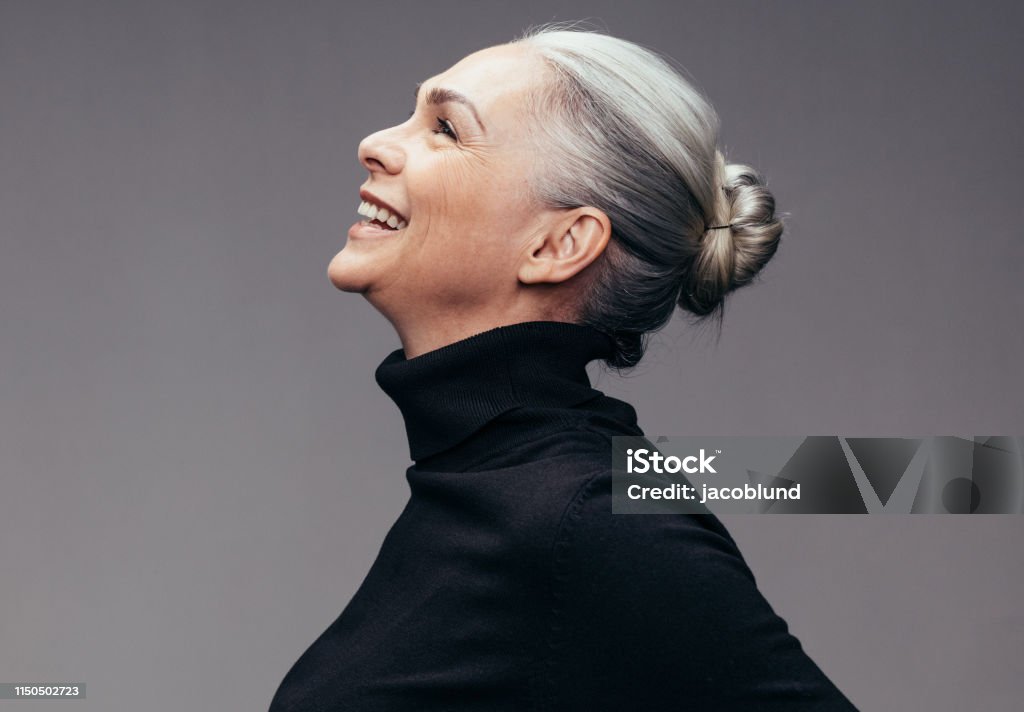 Senior woman looking happy Side view of senior woman laughing on gray background. Profile view of mature woman in black casuals looking happy Women Stock Photo