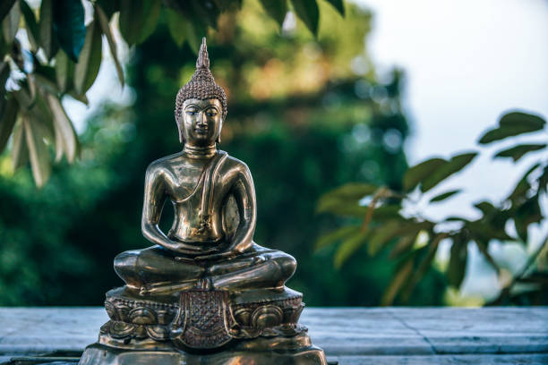 istock Small Golden Buddha Statue surrounded by Green Leaves 1150503316