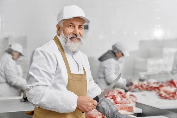 Elderly man working on butchery, cutting meat with knife. stock photo