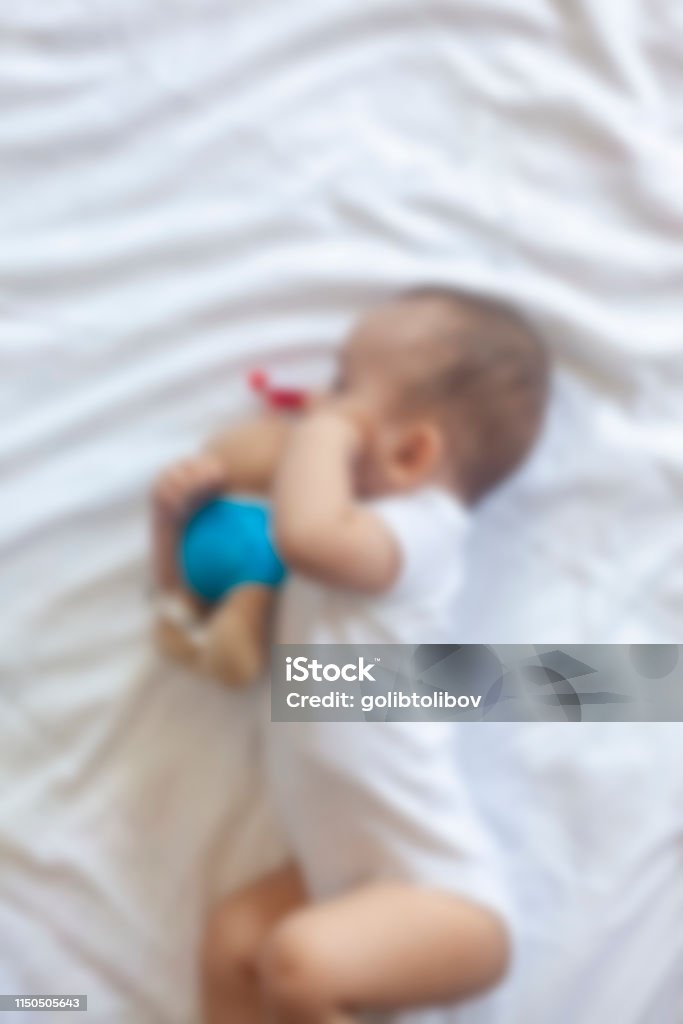 Blurred photo of little baby boy lying playfully in bed Blurred photo of little baby boy lying playfully in bed. Charming 6-7 month little baby in white bodysuit. Baby boy in white bedding. Free space 0-11 Months Stock Photo