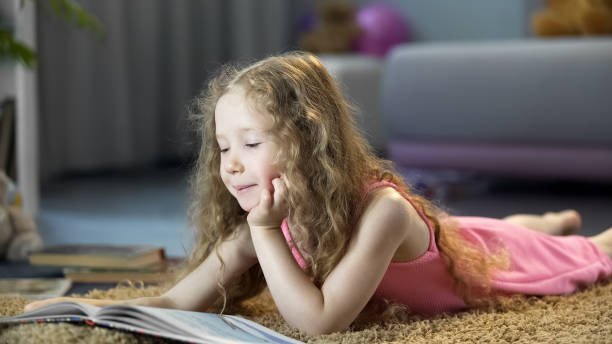 istock Cute little girl reading adventurous book, lying on floor, spending leisure time 1150510023