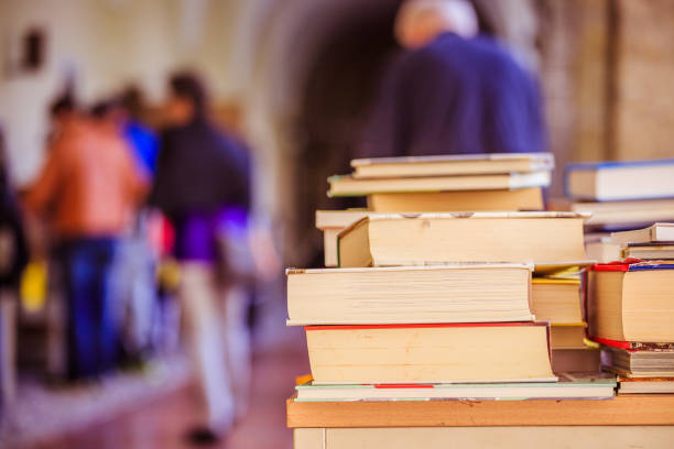 Stack of books, blurry background: Charity book flea market, outdoors. Text space.