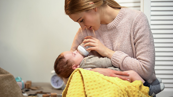 Young mother feeding infant from bottle, problems with breast feeding, mastitis