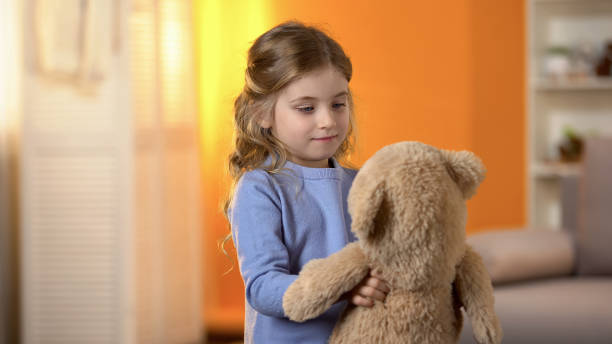 幸せな金髪の巻き毛の少女は、お気に入りのテディベア、子供の頃と遊んで - child little girls shy standing ストックフォトと画像