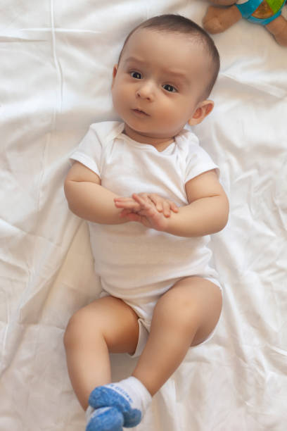 6-8 month old baby boy lying playfully in bed 6-8-month-old baby boy lying playfully in bed. Charming 6-7 month little baby in white bodysuit. Baby boy in white bedding. Free space 6 9 months stock pictures, royalty-free photos & images