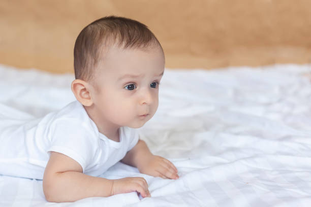 6-8 month old baby boy lying playfully in bed 6-8-month-old baby boy lying playfully in bed. Charming 6-7 month little baby in white bodysuit. Baby boy in white bedding. Free space 6 9 months stock pictures, royalty-free photos & images