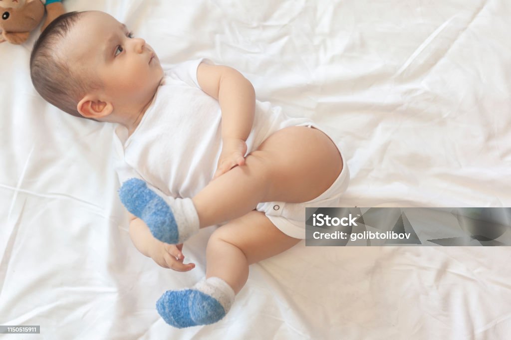 6-8 month old baby boy lying playfully in bed 6-8-month-old baby boy lying playfully in bed. Charming 6-7 month little baby in white bodysuit. Baby boy in white bedding. Free space 0-11 Months Stock Photo