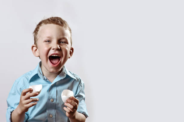 boy in a light shirt holding a shell from the egg and smiling on a light background
