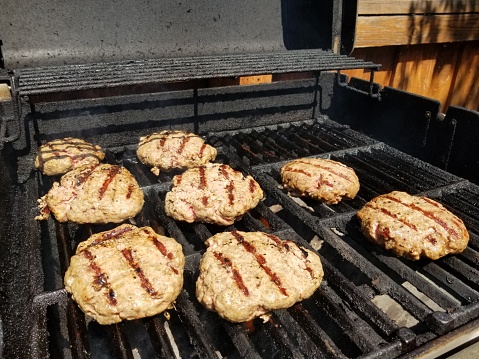 Close-up of several rows of burgers with grill marks cooking on a backyard barbecue grill, September 3, 2018