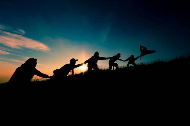 istock silhouette on Group of people helping each other hand by hand on summit with leader hander Thailand Flag during sunset background. Abstract concept of teamwork and success 1150524701