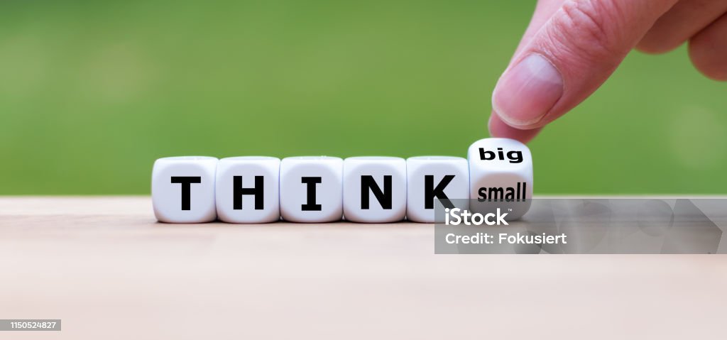 Hand turns a dice and changes the expression "think small" to "think big". Large Stock Photo