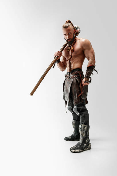Serious long hair and muscular male model in leather viking's costume with the big mace cosplaying isolated on white studio background. Full-length portrait. Fantasy warrior, antique battle concept.