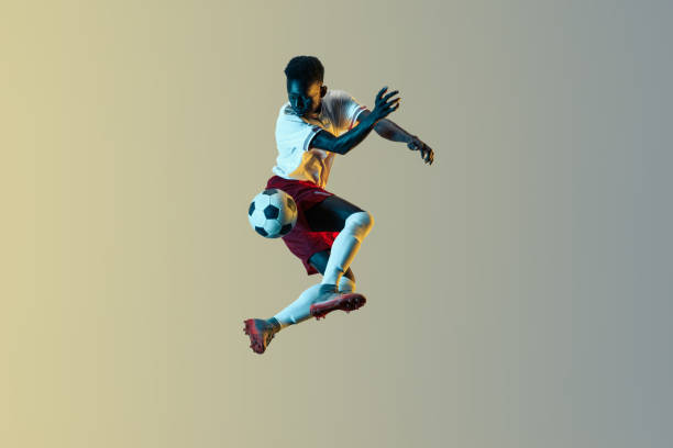 jugador de fútbol masculino patada pelota en salto aislado en fondo degradado - stunt fotografías e imágenes de stock