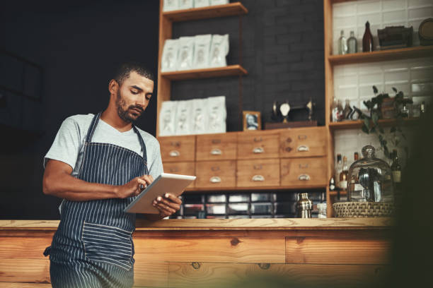 istock Young man in apron using digital tablet at his cafe 1150527972