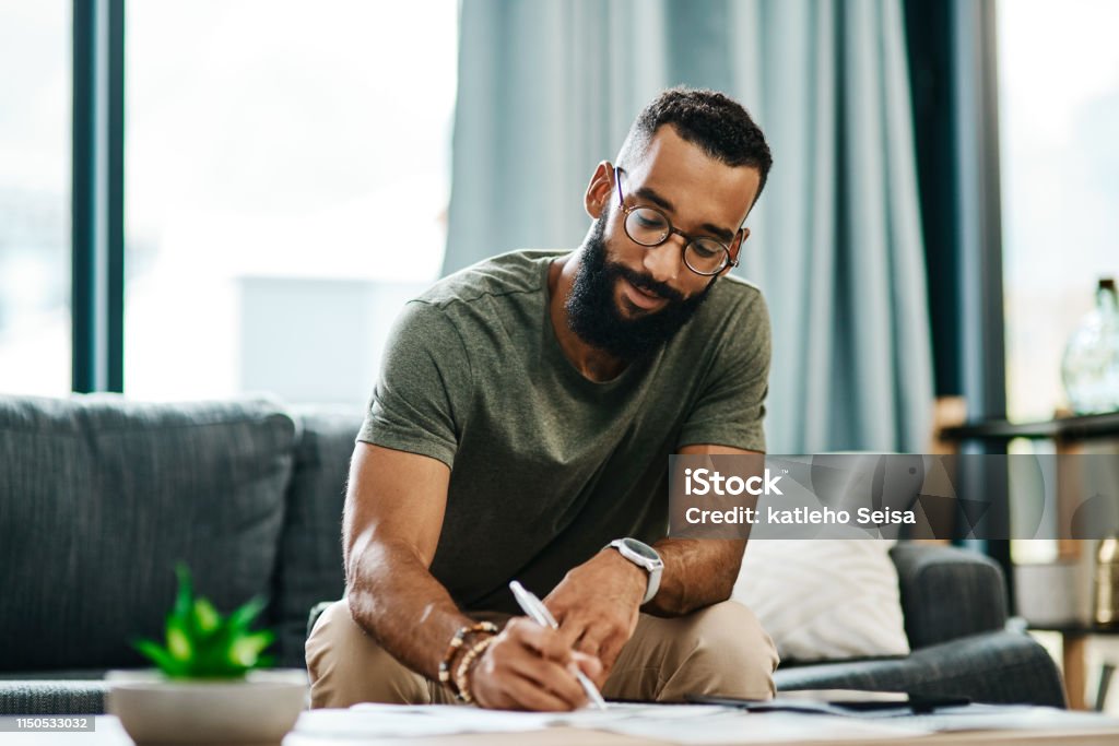 He knows exactly where his money goes Shot of a young man going over his finances at home Writing - Activity Stock Photo