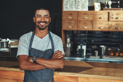 Successful smiling male owner with his arm crossed standing at counter in coffee shop