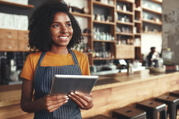 istock Young female owner holding digital tablet in her cafe looking aw 1150533601