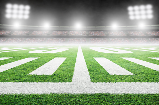 Close up of American football stadium field with yard line markings and spotlight with blurred background and copy space. Fictitious stadium created in Photoshop.