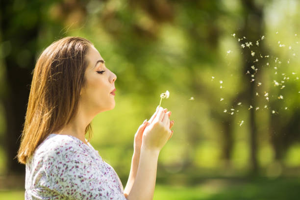 istock Beautiful young woman blowing dandelion 1150536678