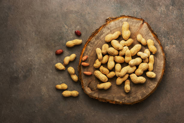 istock Peanuts on a cutting board stump, brown dark background. Top view, flat lay. 1150537218