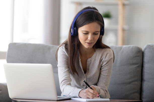 istock Woman in headphones sitting on couch e-learning writing notes 1150540117
