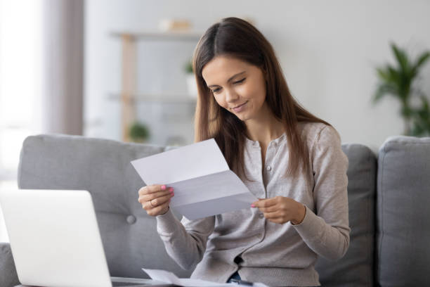 istock Young attractive woman sitting on couch smiling reading letter 1150540166