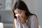 Sick young woman holding tissue and blowing her running nose
