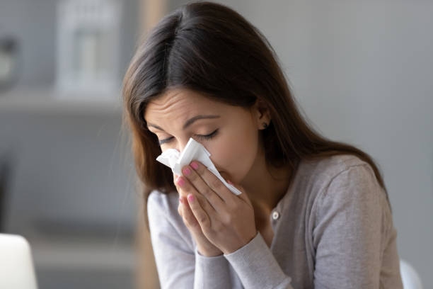 sick young woman holding tissue and blowing her running nose - allergy sneezing cold and flu flu virus imagens e fotografias de stock