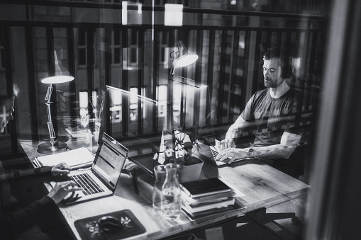 view through window pane on two men working at desk in the office at night