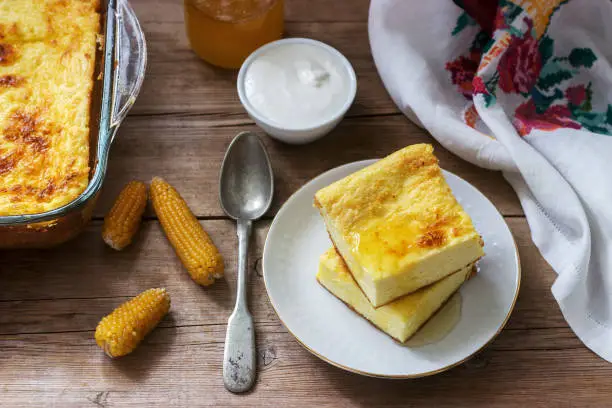 Traditional Romanian or Moldavian cottage cheese casserole with cornmeal, served with honey and sour cream. Rustic style, selective focus.