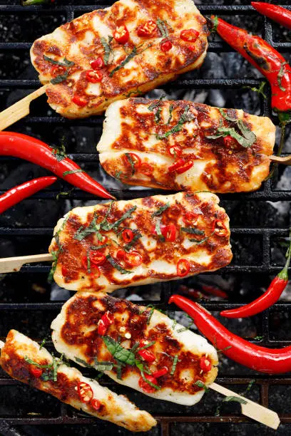 Grilled halloumi cheese with the addition of mint and chilli pepper while grilling outdoors, top view.  Delicious, vegetarian, grilled snack