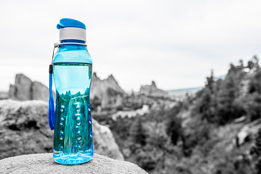 Aqua Blue Fitness Water Bottle Sitting Upon Rock with Mountains in Background. Environmental concept. Fitness concept. Health concept.